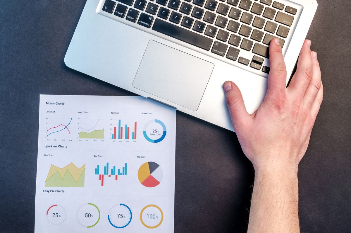A hand on a laptop next to a printed sheet of analytics charts, reviewing store data before a migration
