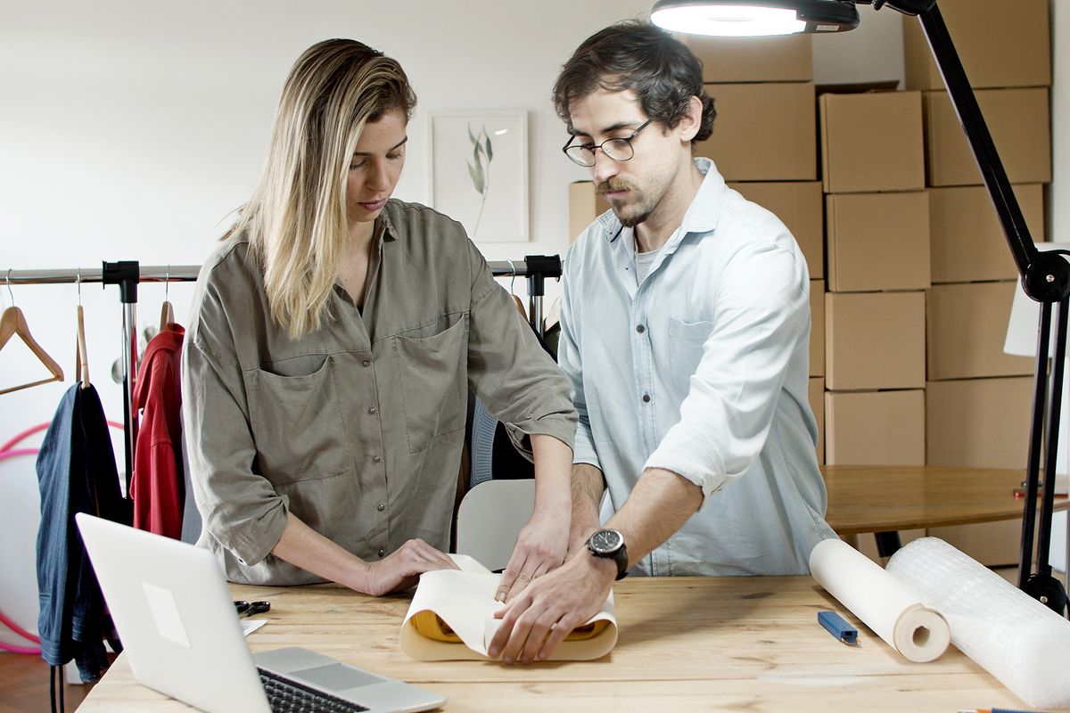 Two people running a small online store, packing an order at a workbench with a laptop and shipping boxes
